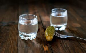 Две рюмки водки и соленый огурец на столе